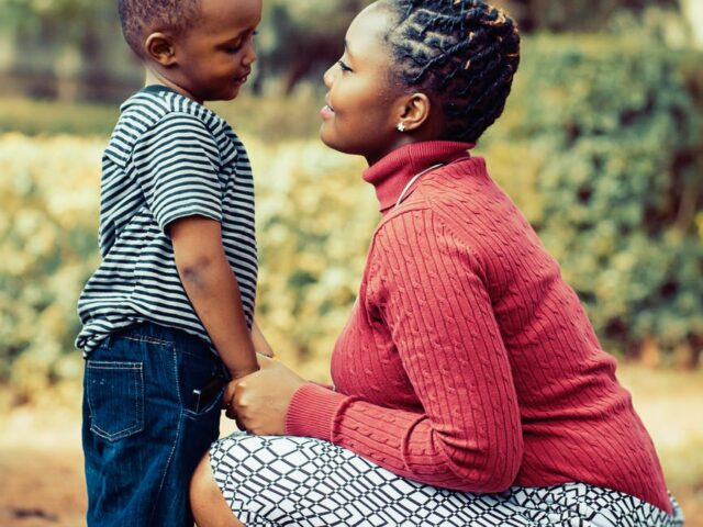 tilt shift lens photography of woman wearing red sweater and white skirt while holding a boy wearing white and black crew neck shirt and blue denim short